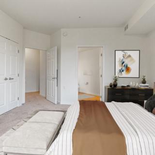 A modern bedroom with a neatly made bed, artwork on the wall, and a dresser.