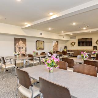 A well-lit community room with tables and chairs arranged neatly, adorned with floral centerpieces.