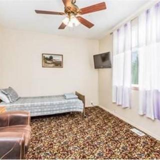 A simple bedroom with a single bed, patterned carpet, ceiling fan, and wall-mounted television.