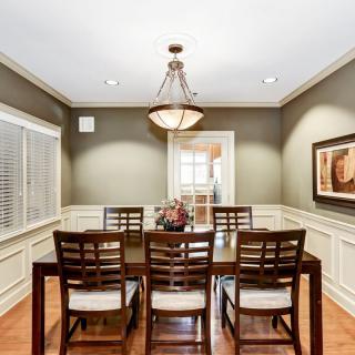 A well-lit dining room with a wooden table and chairs under a traditional chandelier.