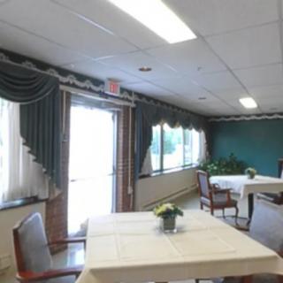 A well-lit dining area with tables, chairs, and large windows adorned with green curtains.