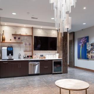 A modern kitchenette with a chandelier and wall-mounted television, featuring minimalist decor and artwork.