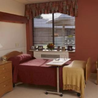 A cozy hospital room with a bed by the window and wooden furniture.