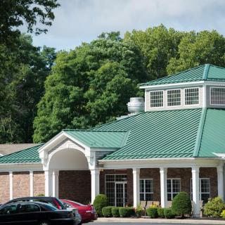 A building with a green roof and white columns, surrounded by trees, with cars parked in front.