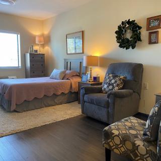 A cozy bedroom with a bed, armchair, and warm lighting.