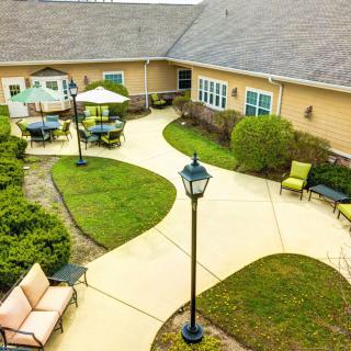 A view of a courtyard with pathways and outdoor seating areas, surrounded by greenery and a building.