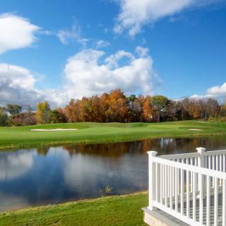 A scenic view of a golf course with a lake, surrounded by autumn trees under a clear blue sky.