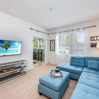 A bright and modern living room featuring a blue sectional sofa, television, and abundant natural light.