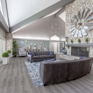 A spacious living room with modern decor featuring a stone fireplace, vaulted ceiling, and a large circular clock as a focal point.
