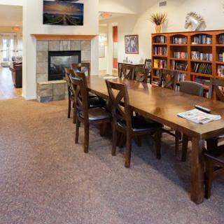 A cozy dining area featuring a long wooden table surrounded by chairs, with a bookcase and fireplace in the background.