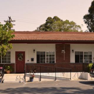 A quaint single-story building with a red door and surrounded by trees.