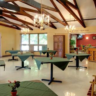 An empty restaurant dining area with tables set for service, featuring chandeliers and wooden ceiling beams.