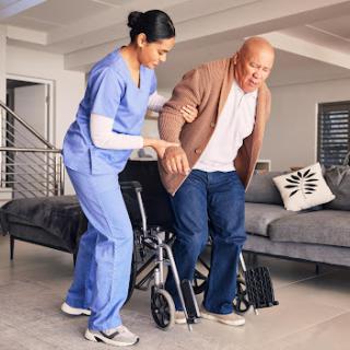A caregiver assists an elderly person in getting up from a wheelchair in a home setting.