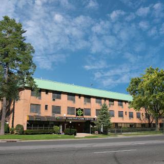 A modern hotel with a green roof set against a sunny blue sky, surrounded by greenery.