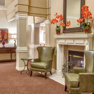 A cozy living room with green armchairs, a fireplace, and vibrant flower decorations.