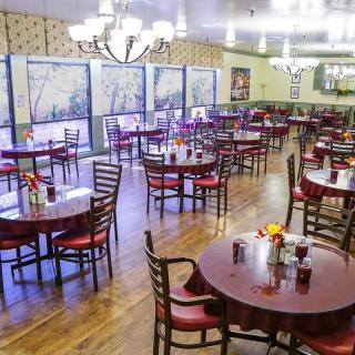 An empty restaurant dining area with neatly arranged tables and chairs, elegant lighting, and decorative elements.