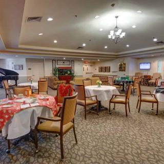 A cozy dining room with decorated tables and chairs, featuring a chandelier and warm ambiance.