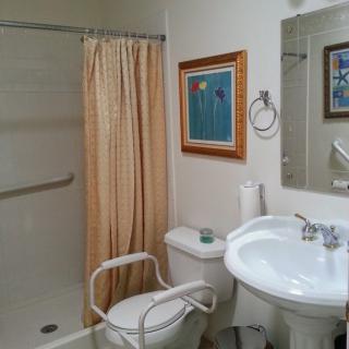 A bathroom with a walk-in shower, beige shower curtain, pedestal sink, and framed artwork on the wall.