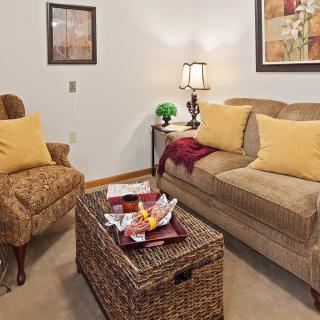 A cozy living room with a sofa, armchair, and a wicker coffee table adorned with books and snacks.