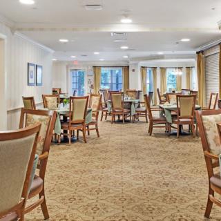 A spacious dining room with neatly arranged tables and chairs, carpeted flooring, and natural light coming through the windows.