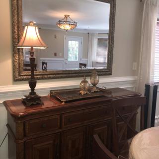 A well-decorated living room corner featuring a wooden sideboard with a lamp and decorative items, complemented by a large wall mirror.