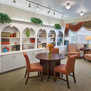 Cozy library room with shelves and a central table surrounded by chairs.