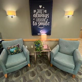 A cozy waiting area featuring two blue chairs, a small table with greenery, and an inspirational quote on the wall.