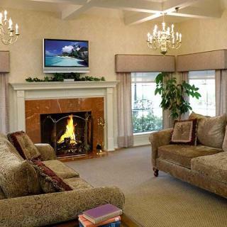 A cozy living room featuring a fireplace, comfortable sofas, chandeliers, and a television mounted above the mantel.