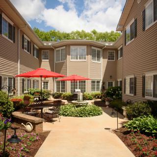 A well-maintained courtyard with outdoor seating and red umbrellas, surrounded by residential buildings on a sunny day.
