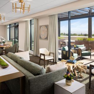 A spacious and luxurious living room with modern furnishings, featuring large windows that open to a balcony with outdoor seating.