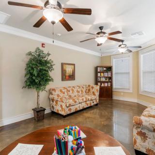 A cozy living room with floral sofas, ceiling fans, and a bookshelf against a hardwood floor.