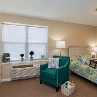 A cozy bedroom with a bed, teal armchair, and decorative elements under soft lighting.