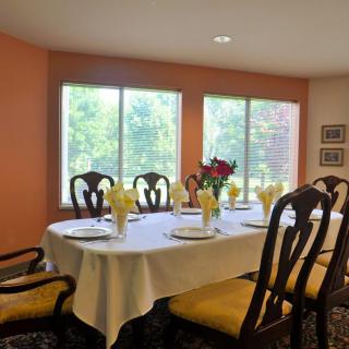 A well-set dining table with yellow napkins and a floral centerpiece in a bright room with large windows.