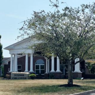 A stately building featuring classic architectural elements with columns, set against a backdrop of greenery.