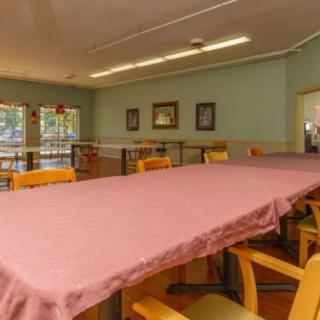 An empty dining room with a long table covered in a pink tablecloth and surrounded by chairs.
