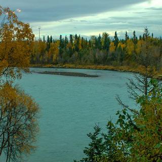 A scenic view of a river surrounded by autumn trees and a cloudy sky.