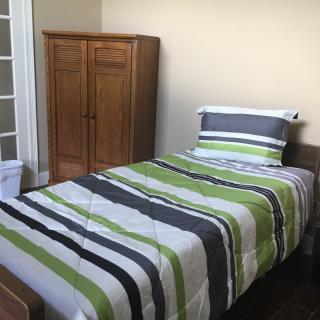 A cozy bedroom featuring a single bed with striped bedding and a wooden wardrobe.