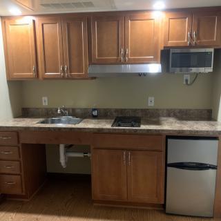 A compact kitchen with wooden cabinets, a sink, microwave, and small refrigerator.