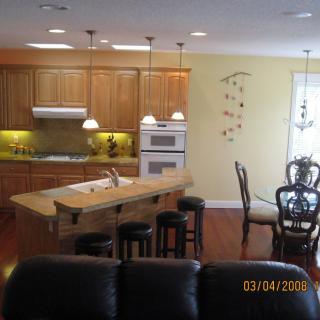 A modern kitchen and dining area featuring wooden cabinets, an island with stools, and pendant lighting.
