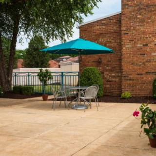 A cozy patio setup with a table, chairs, and a teal umbrella, surrounded by brick walls and greenery.