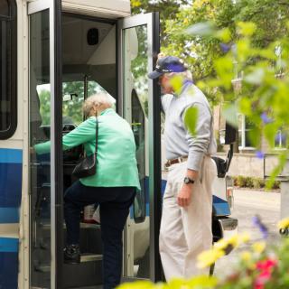 Elderly individuals boarding a public bus in an urban setting.