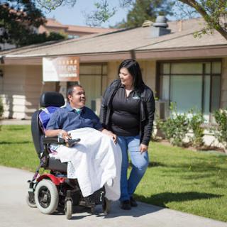 A caregiver and a person in a wheelchair share a moment outside a residential home.