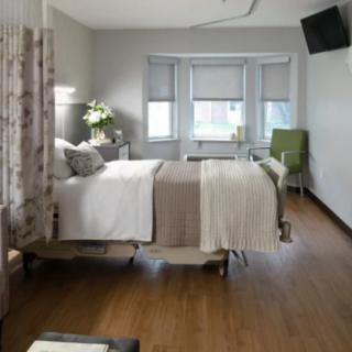 A modern hospital room with a comfortable bed, television, and seating area.