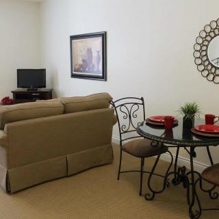 A cozy living room with a small dining area, featuring a sofa, TV, round table with chairs, and decorative items like a mirror and painting.