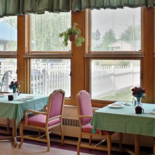A cozy dining area with tables covered in green tablecloths, set by large windows allowing natural light to fill the room.