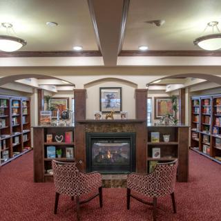 A cozy library with bookshelves, a fireplace, and two chairs arranged in the center.
