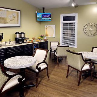 A cozy seating area with tables and chairs, featuring a coffee station and a wall-mounted television.