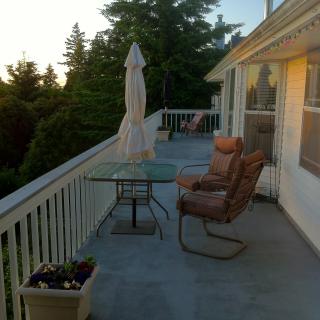 A peaceful balcony setting with chairs, a table, and an umbrella overlooking lush trees at sunset.