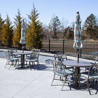 A sunny outdoor patio with tables, chairs, and umbrellas surrounded by trees and a fence.