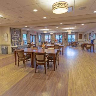 An empty dining room with wooden floors and neatly arranged tables and chairs.